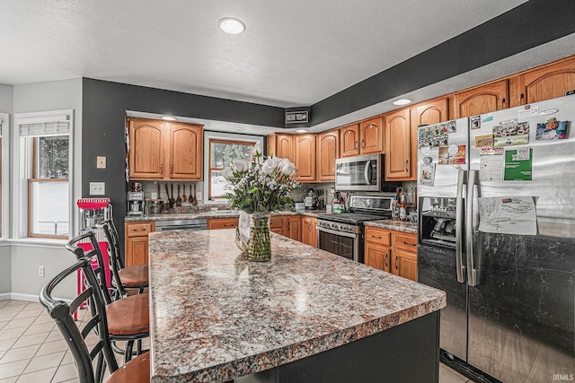 kitchen featuring a textured ceiling, a kitchen island, light tile patterned flooring, and stainless steel appliances