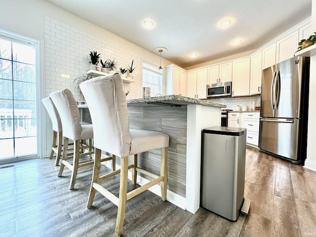 kitchen featuring a breakfast bar, decorative light fixtures, light stone countertops, appliances with stainless steel finishes, and white cabinets