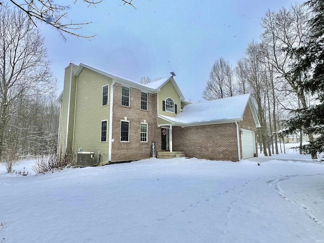 snow covered rear of property with a garage and central AC