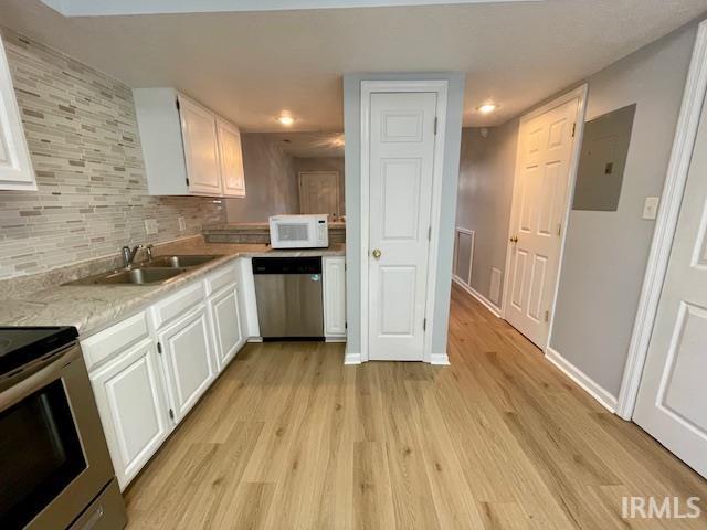 kitchen with stainless steel appliances, white cabinets, electric panel, decorative backsplash, and light wood-type flooring