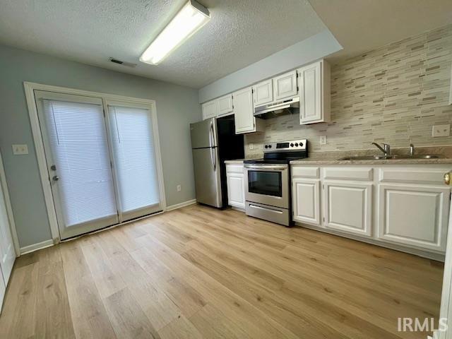 kitchen with light wood-type flooring, sink, appliances with stainless steel finishes, white cabinets, and decorative backsplash