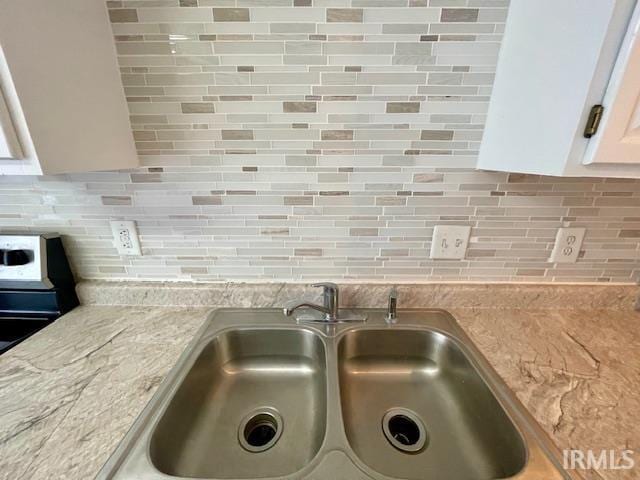 interior details with sink, white cabinetry, light stone countertops, and backsplash