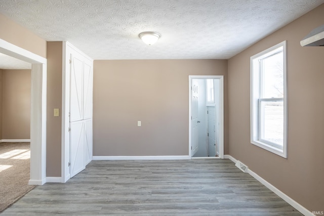 unfurnished room with light hardwood / wood-style flooring and a textured ceiling