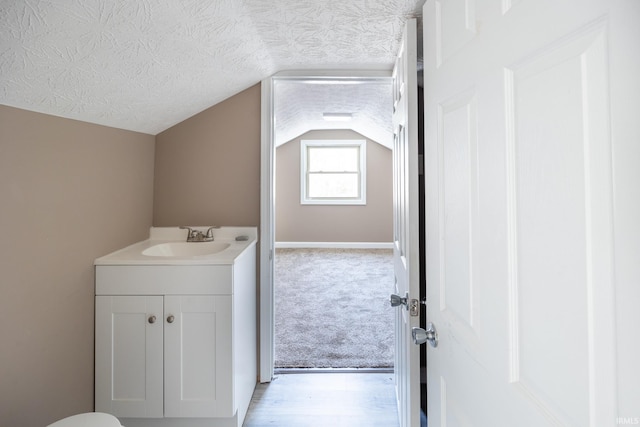 bathroom with a textured ceiling, vanity, and lofted ceiling