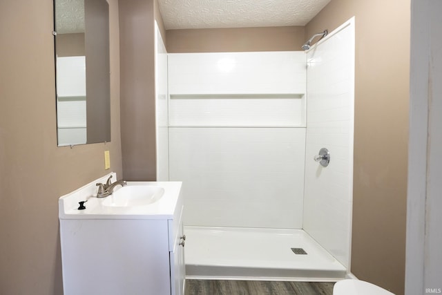 bathroom with a textured ceiling, toilet, vanity, and walk in shower