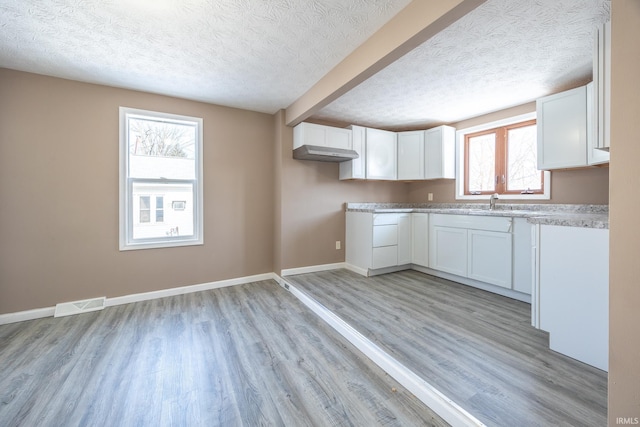 kitchen featuring a textured ceiling, white cabinets, and light hardwood / wood-style flooring