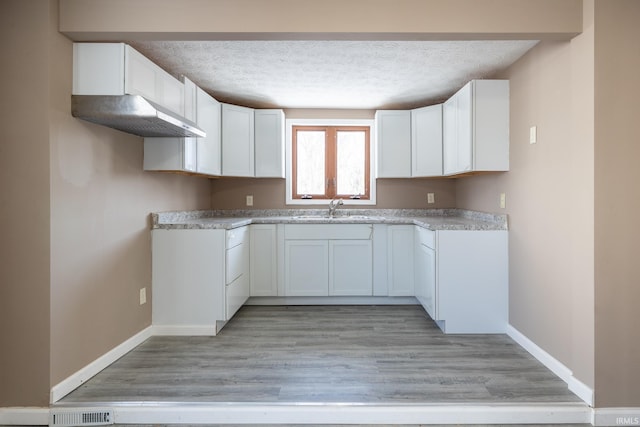 kitchen with white cabinets, light wood-type flooring, sink, and a textured ceiling