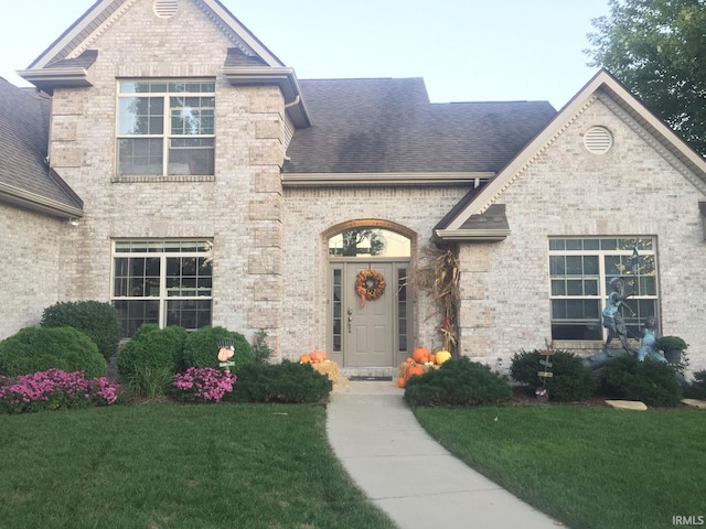 french country inspired facade featuring brick siding, a front lawn, and roof with shingles