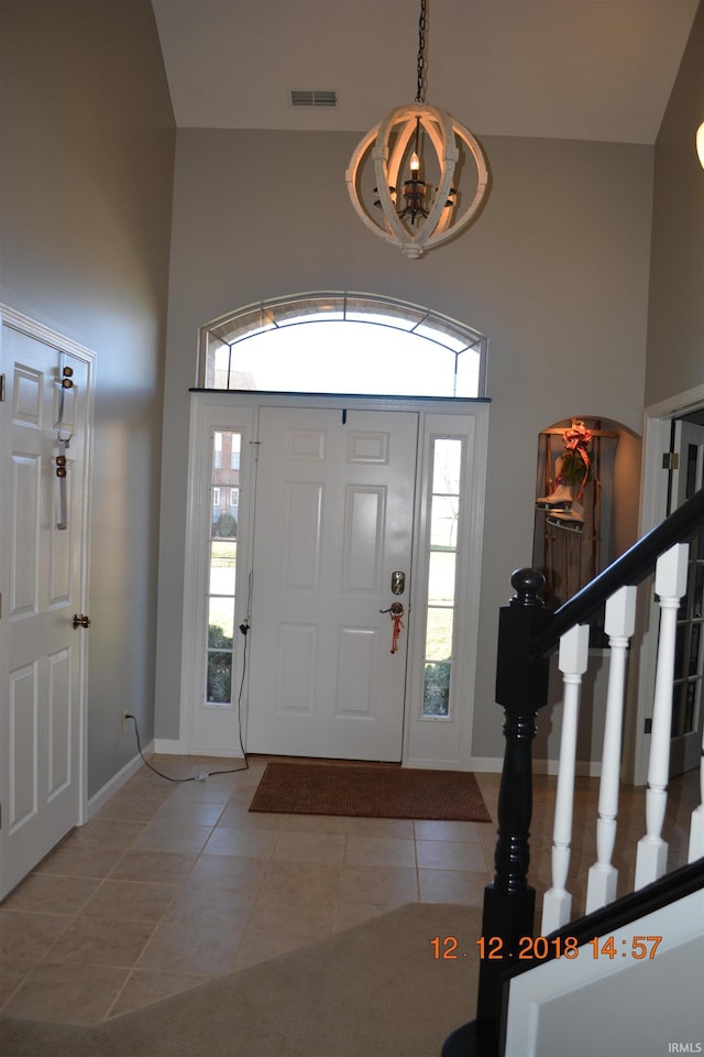 entrance foyer with light tile patterned floors, visible vents, stairway, a towering ceiling, and baseboards