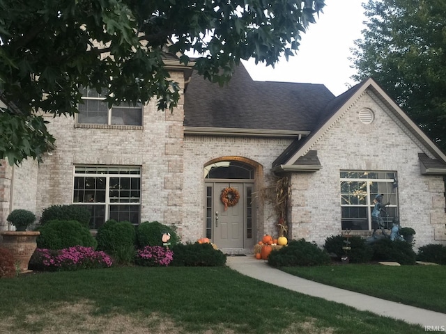 french provincial home featuring brick siding, a front yard, and a shingled roof