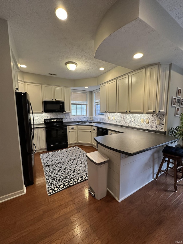 kitchen featuring a peninsula, a breakfast bar, dark wood-style floors, black appliances, and dark countertops