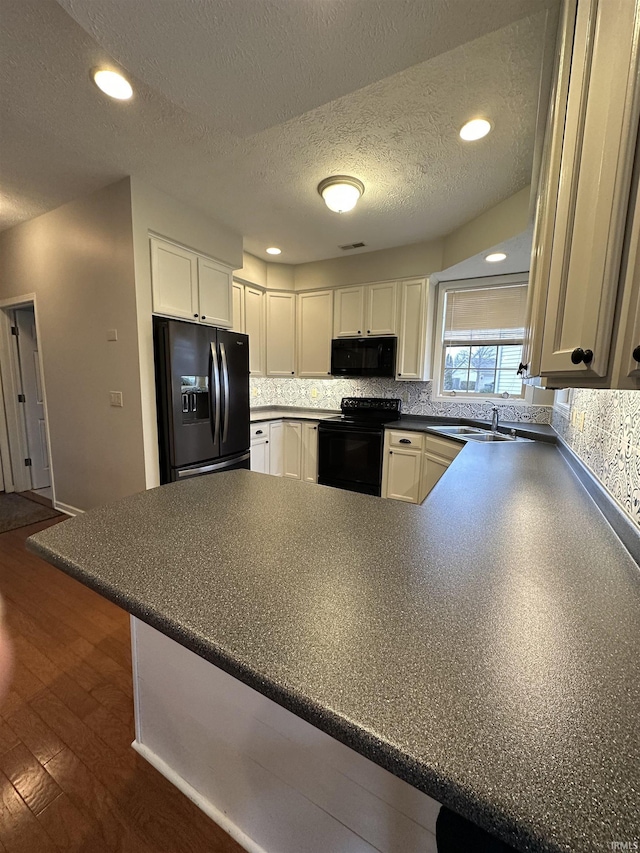 kitchen with tasteful backsplash, white cabinets, dark countertops, a peninsula, and black appliances