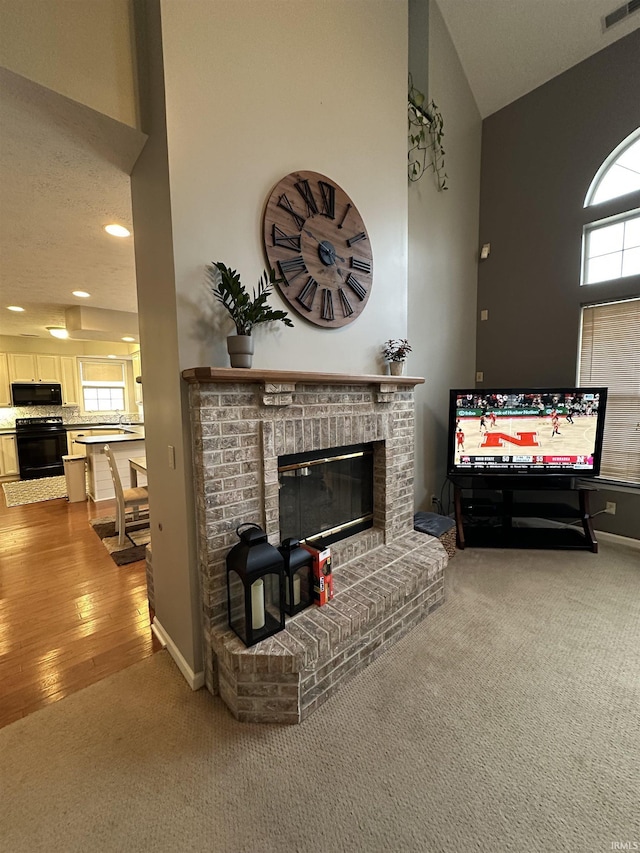 living room with visible vents, baseboards, a towering ceiling, carpet, and a brick fireplace