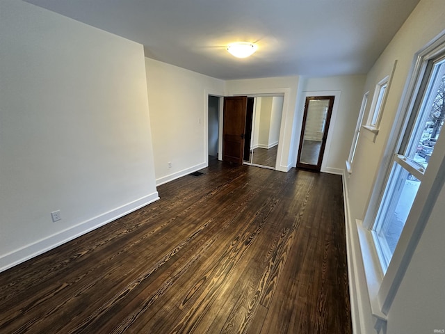 unfurnished room featuring dark wood-style flooring, visible vents, and baseboards