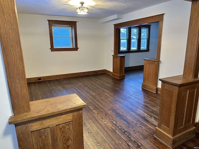 empty room with dark wood-style flooring, a textured ceiling, and baseboards