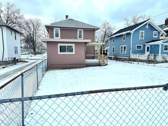 snow covered house with a residential view, fence, and roof with shingles