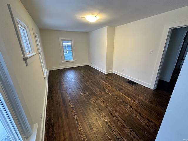 spare room featuring dark wood-type flooring, visible vents, and baseboards