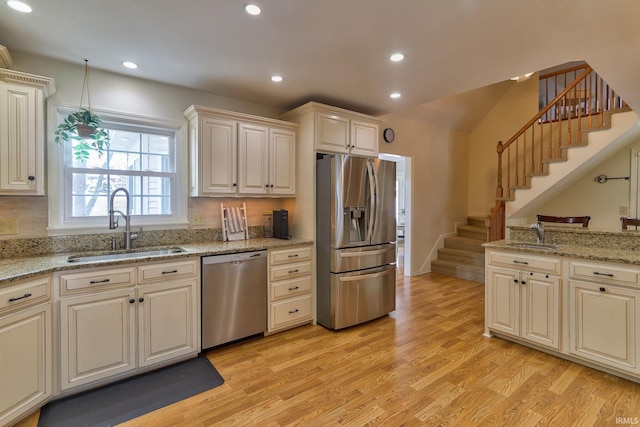 kitchen featuring light wood-type flooring, cream cabinets, sink, light stone counters, and appliances with stainless steel finishes