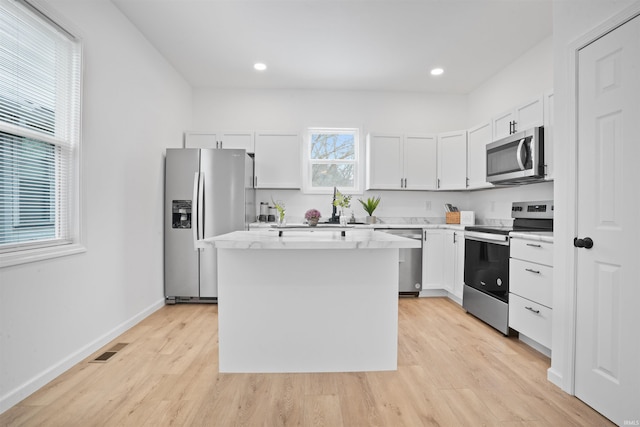 kitchen featuring light wood-type flooring, appliances with stainless steel finishes, white cabinets, and a center island