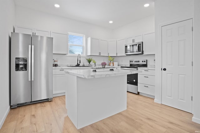 kitchen featuring light hardwood / wood-style flooring, stainless steel appliances, a kitchen island, sink, and white cabinetry