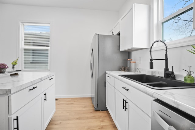 kitchen with light hardwood / wood-style flooring, appliances with stainless steel finishes, sink, white cabinets, and light stone countertops