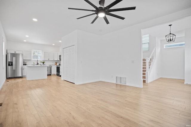 unfurnished living room with ceiling fan with notable chandelier, light hardwood / wood-style flooring, and sink