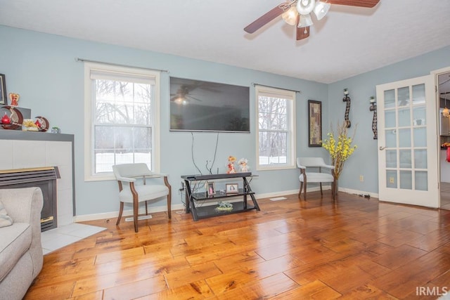 sitting room with light wood-type flooring, a tiled fireplace, and ceiling fan