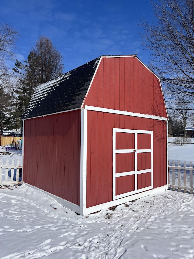 snow covered structure with a barn, fence, and an outbuilding