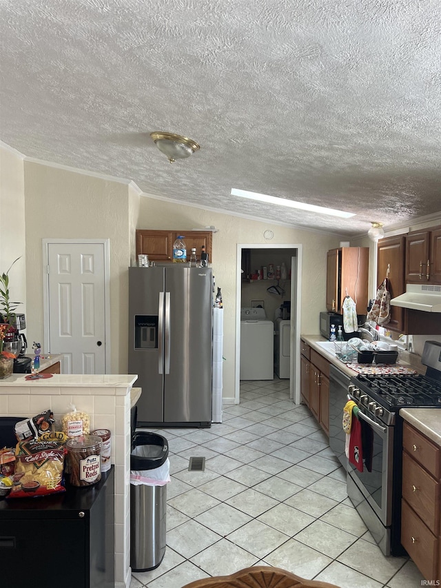 kitchen with washing machine and clothes dryer, light countertops, appliances with stainless steel finishes, brown cabinetry, and under cabinet range hood