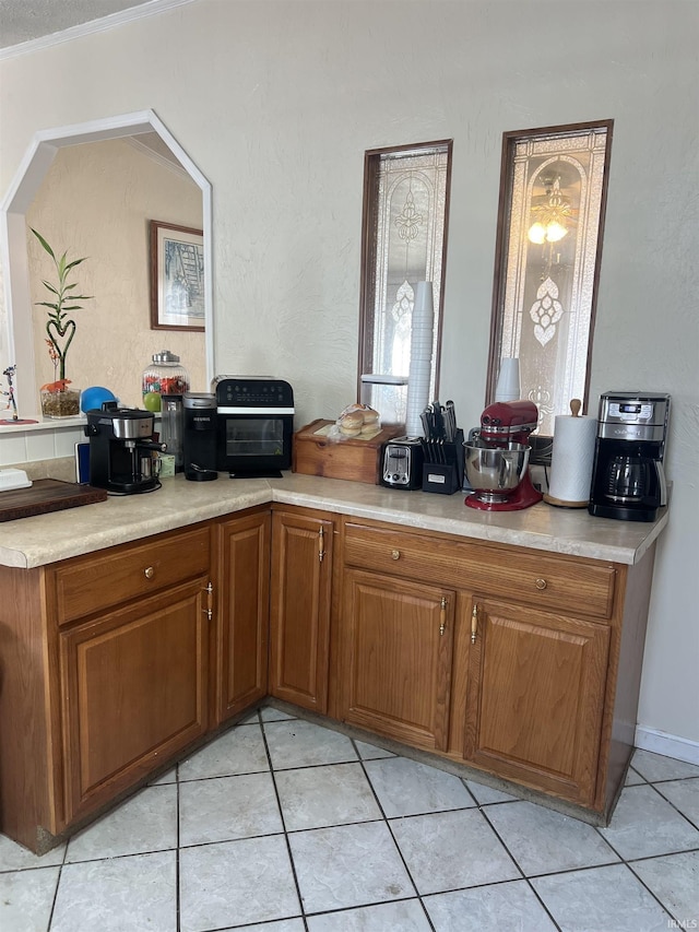 kitchen with brown cabinets, light countertops, ornamental molding, and light tile patterned floors