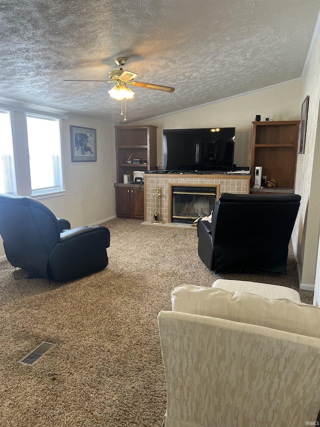 living area with a ceiling fan, a tile fireplace, carpet flooring, and a textured ceiling