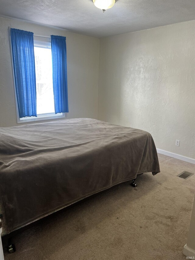 carpeted bedroom featuring visible vents, a textured wall, a textured ceiling, and baseboards