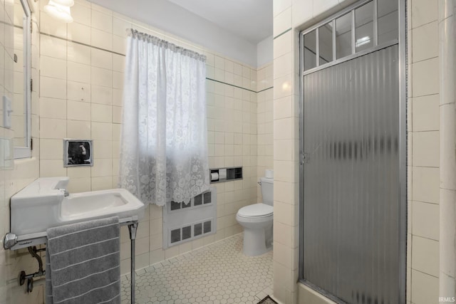 bathroom with tile patterned floors, toilet, tile walls, and a shower with shower door