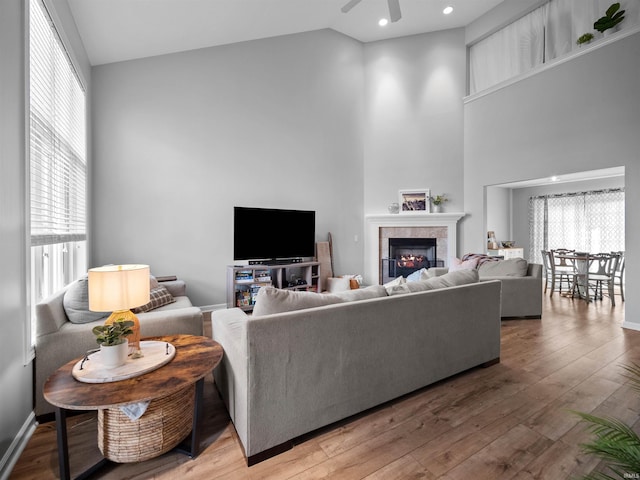 living room featuring high vaulted ceiling, hardwood / wood-style flooring, ceiling fan, and a tiled fireplace