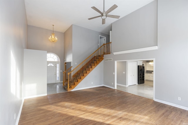 unfurnished living room featuring hardwood / wood-style floors, a towering ceiling, and ceiling fan with notable chandelier