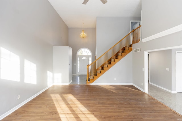 unfurnished living room featuring ceiling fan with notable chandelier, light wood-type flooring, and a high ceiling