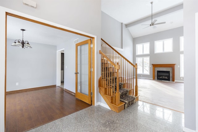 stairs with ceiling fan with notable chandelier, high vaulted ceiling, and a tiled fireplace