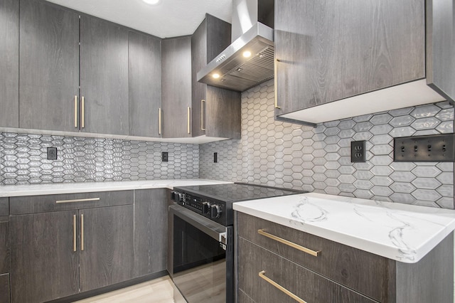 kitchen featuring electric range, light stone countertops, light hardwood / wood-style floors, backsplash, and wall chimney exhaust hood