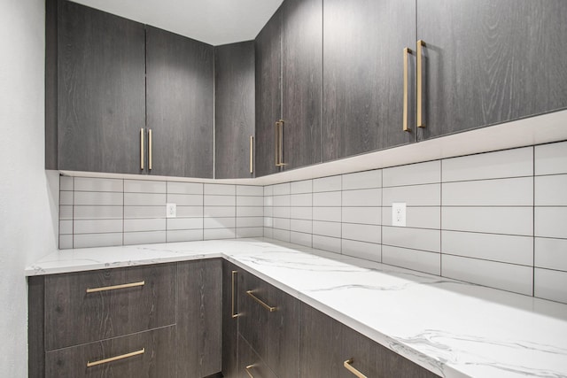 kitchen featuring dark brown cabinets, tasteful backsplash, and light stone counters