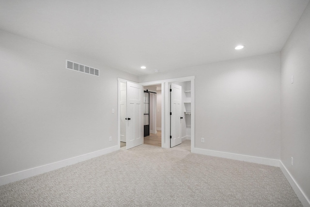 unfurnished bedroom with a walk in closet and light colored carpet