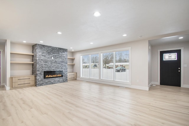 unfurnished living room with light wood-type flooring, built in shelves, and a stone fireplace