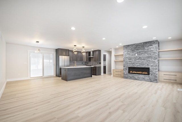 unfurnished living room with sink, light hardwood / wood-style flooring, and a stone fireplace