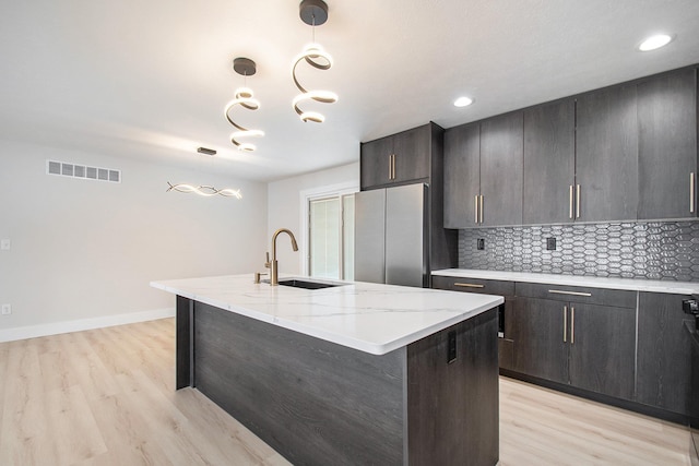 kitchen with a kitchen island with sink, decorative light fixtures, stainless steel refrigerator, sink, and tasteful backsplash