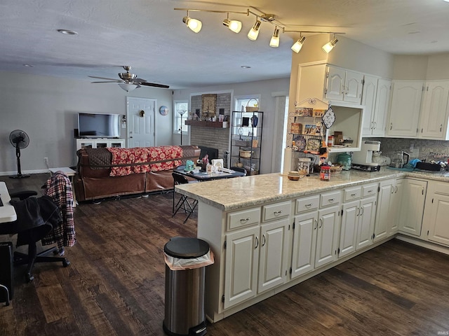 kitchen featuring a fireplace, dark wood-type flooring, kitchen peninsula, and white cabinets