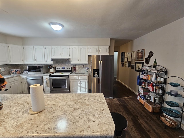 kitchen with white cabinetry, stainless steel appliances, light stone countertops, dark hardwood / wood-style floors, and decorative backsplash