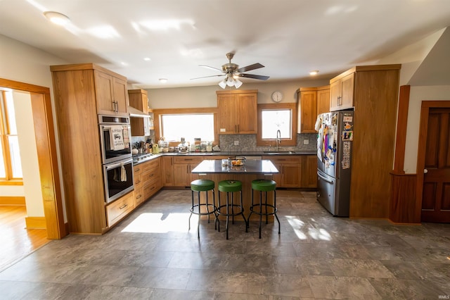 kitchen with a kitchen bar, sink, backsplash, a center island, and stainless steel appliances