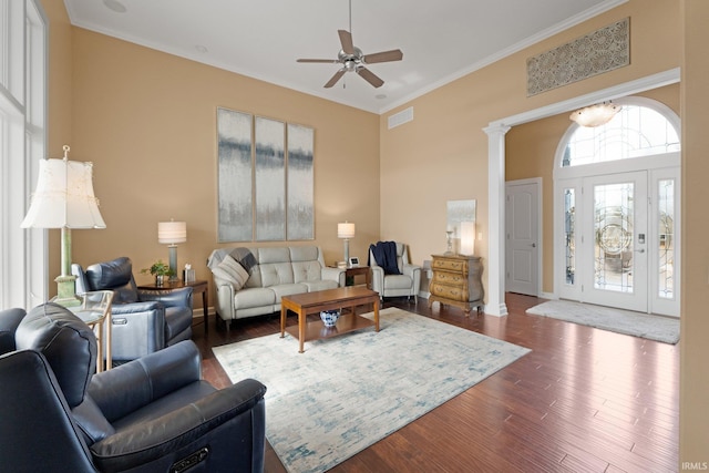 living room featuring decorative columns, a towering ceiling, ornamental molding, ceiling fan, and dark hardwood / wood-style floors