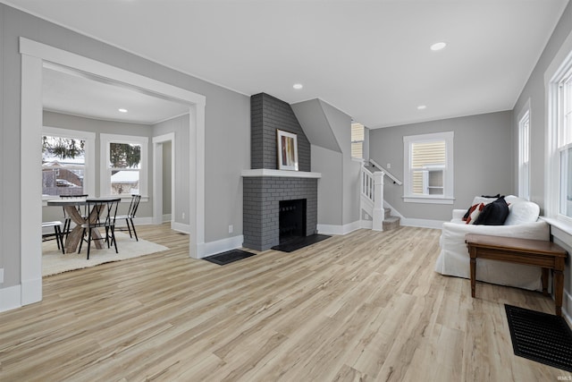 living room featuring stairs, a fireplace, light wood-style floors, and baseboards