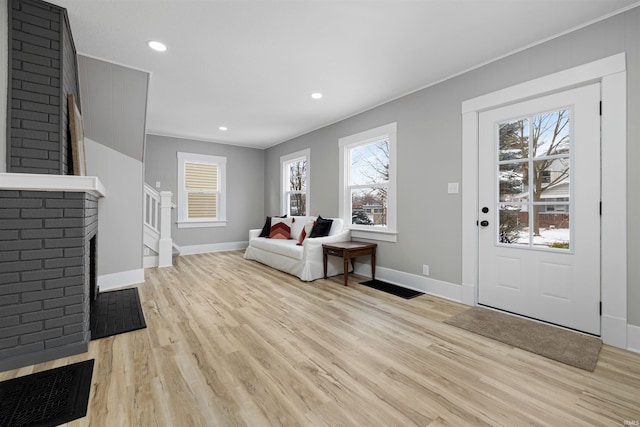 foyer entrance with stairway, a brick fireplace, light wood-type flooring, and baseboards