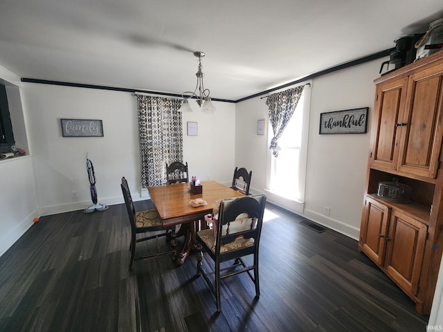 dining area with dark wood-type flooring, crown molding, and a chandelier